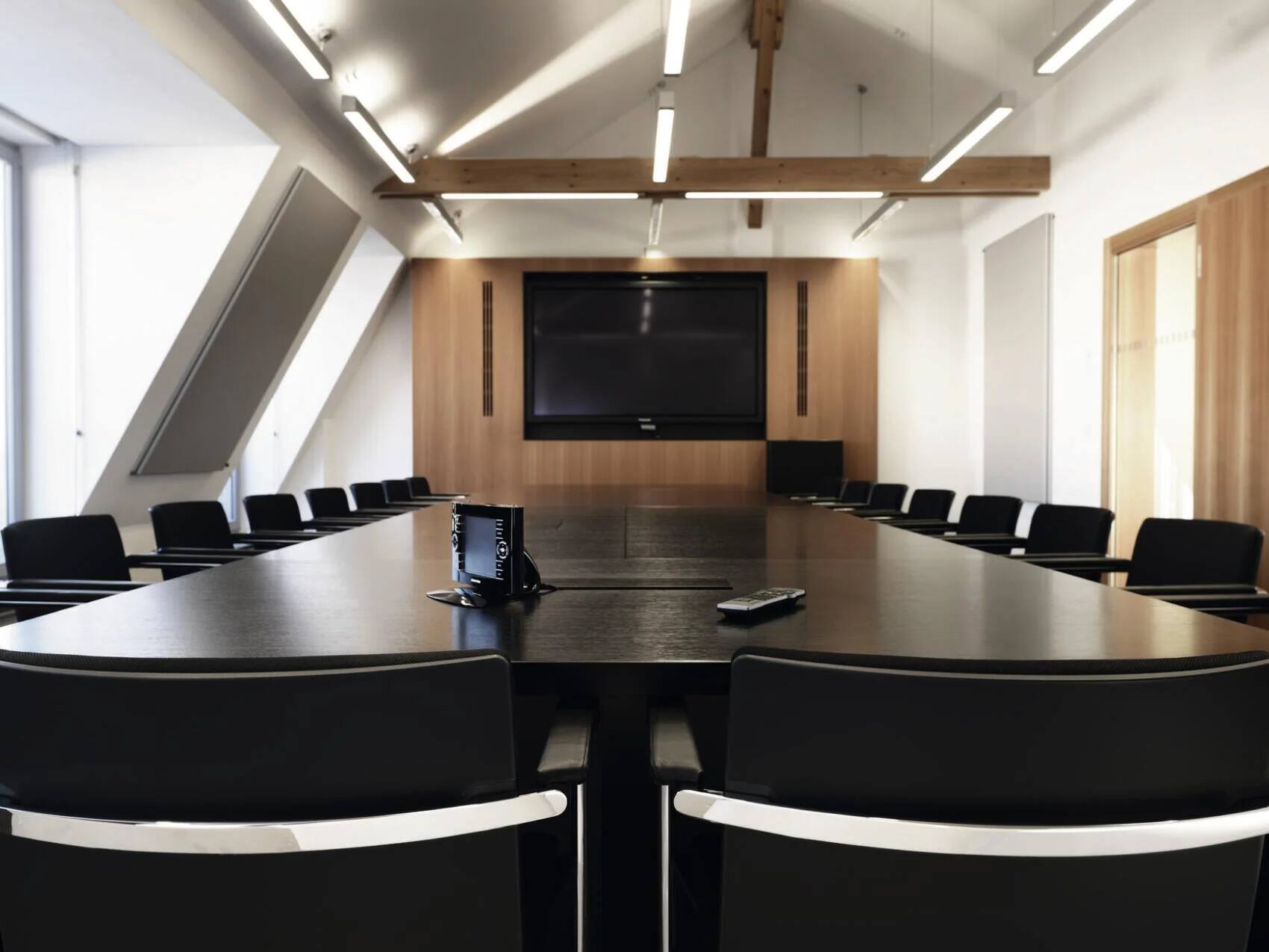Moderner Konferenzraum mit großem Tisch, Stühlen und Präsentationsscreen