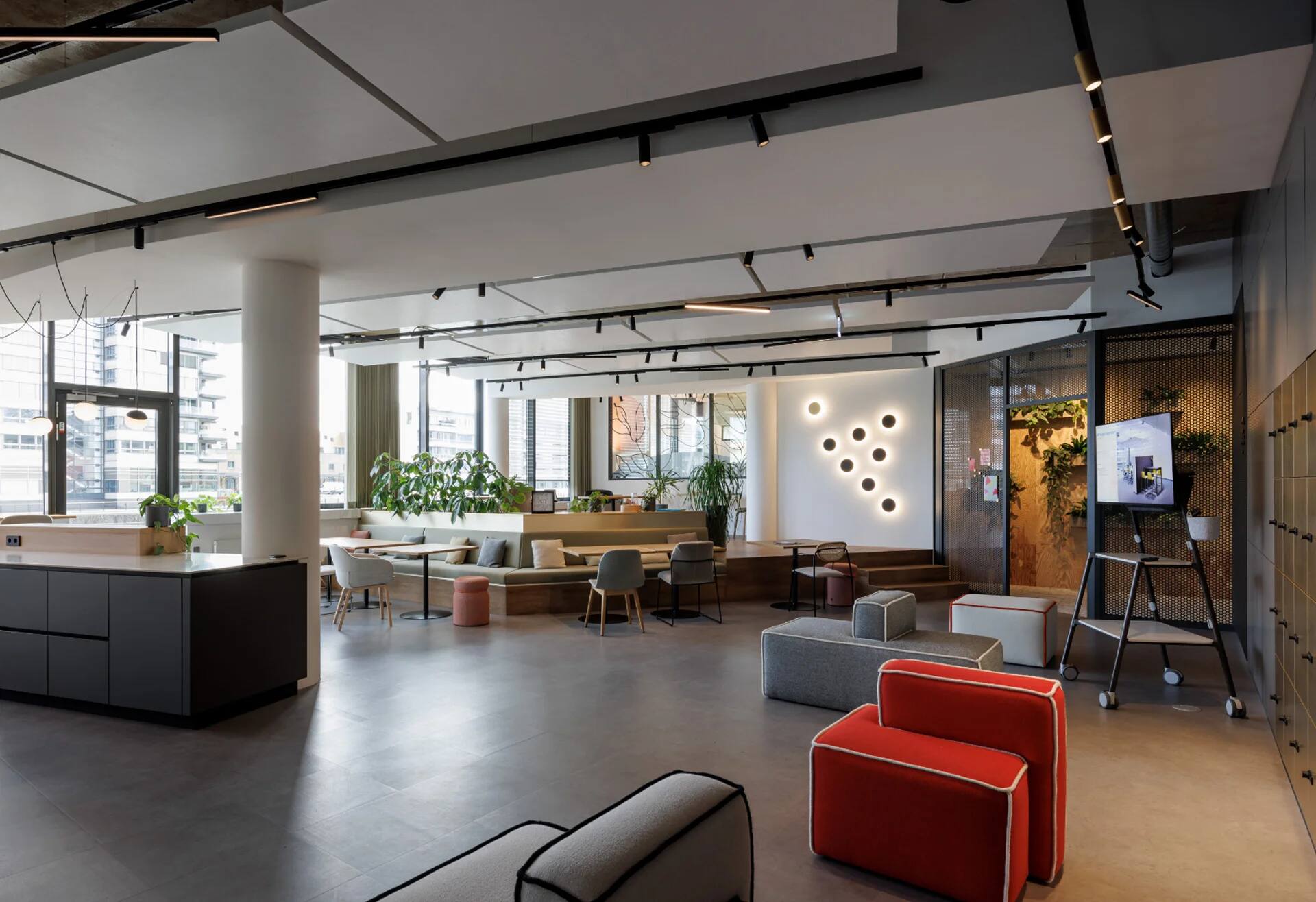 Moderner Coworking-Space mit Lounge, Pflanzen, Sitzinseln und Monitorwand